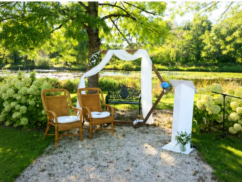 Arche de mariage en bois avec voilage blanc et chaises rotin près d'un étang en Loire-Atlantique