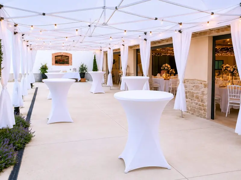 Allée de barnums blancs avec mange-debout nappés et guirlandes guinguette pour un cocktail de mariage en Loire-Atlantique